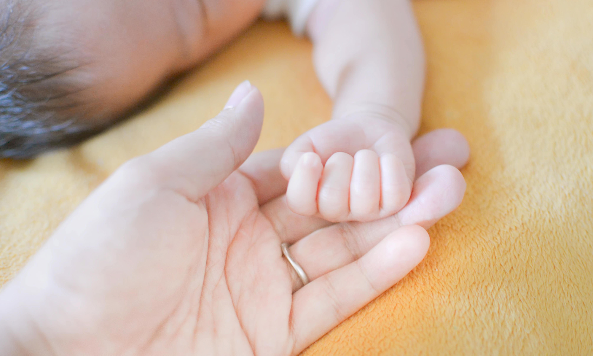眠る赤ちゃんと手をつなぐ大人の手